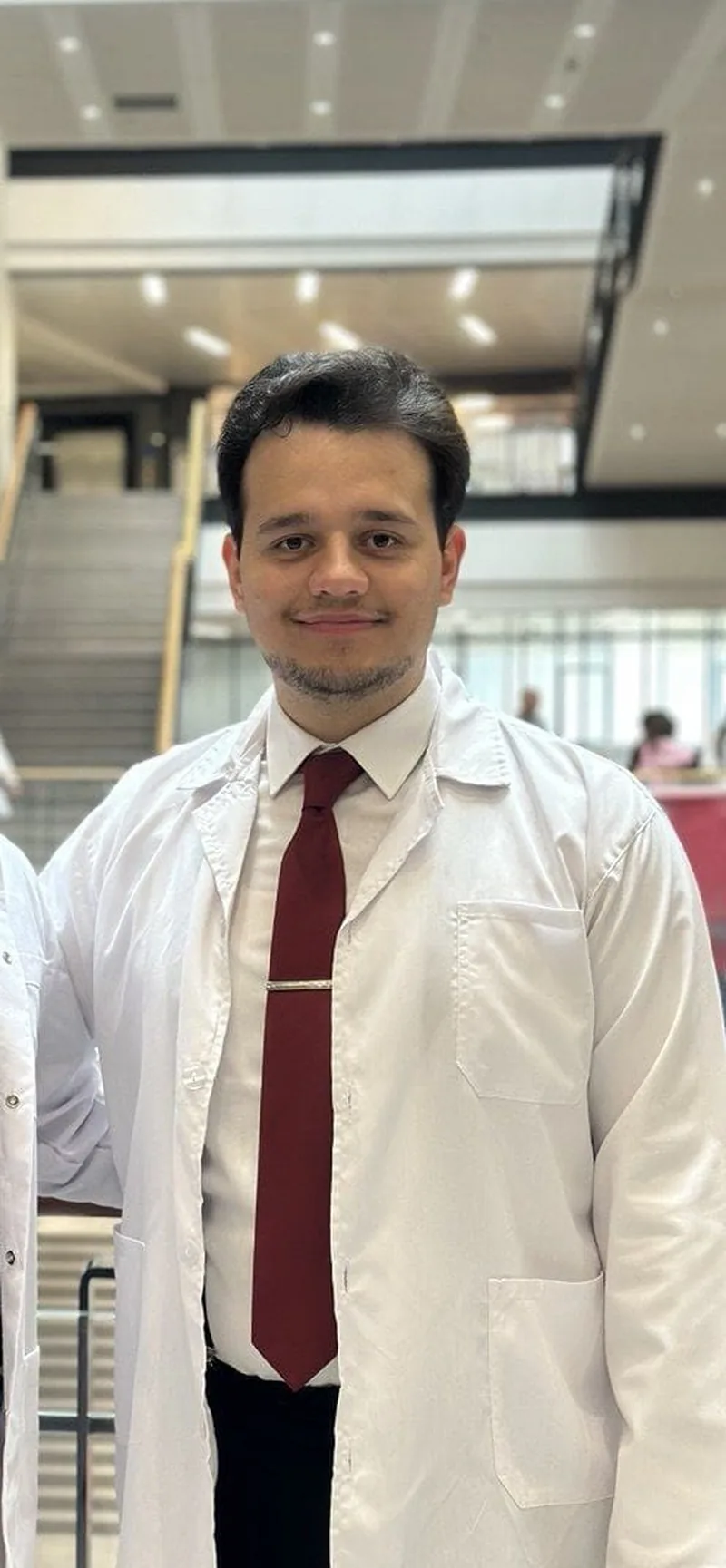 Omid Aslani Damirchi wearing a white clinical coat in an indoor academic setting